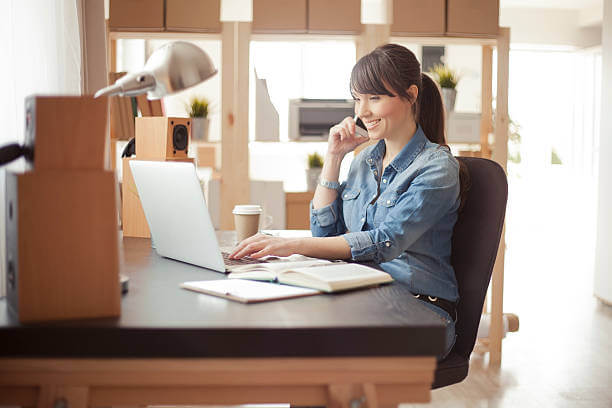 Young woman working at her home office. Office consists of wooden shelves and modern wooden table.