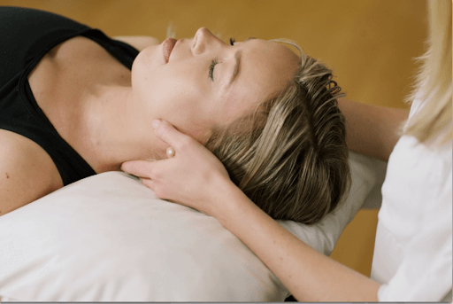 a physiotherapist massaging a client’s neck while the client is laying down and has her eyes closed