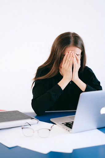 woman at desk covering her face with hands with laptop in front