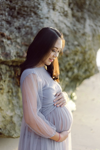 A pregnant woman in dress smiling down at baby bump