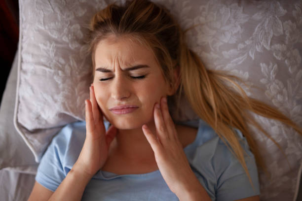 A woman lying down on bed, touching her jaw with teeth grinding