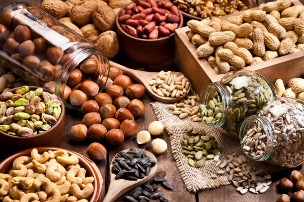 wood table filled with a large assortment of nuts like pistachios, hazelnut, pine nut, almonds, pumpkin seeds, sunflower seeds, peanuts, cashew and walnuts.