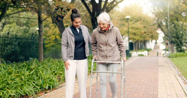 Senior woman with walker. Walking with physiotherapist and in a public garden